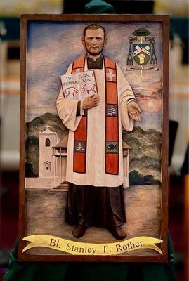 Large item of Blessed Stanley Rother in front of the church he was a priest at when he was martyred.