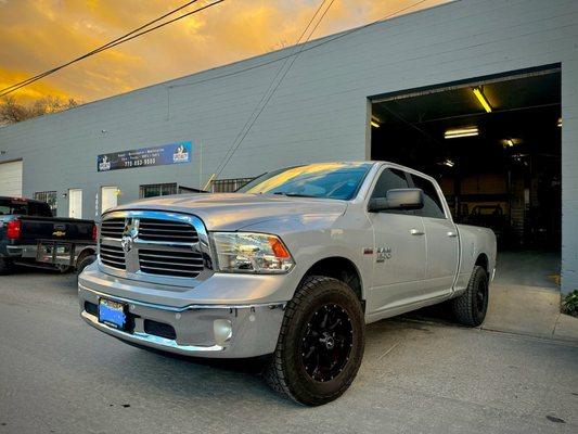 Ram Classic with black rims and leveling kit in front of Specialty Automotive shop.