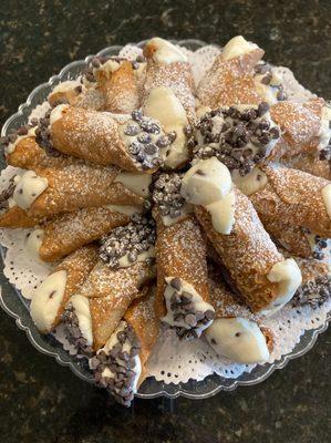 A plate of fresh cannoli desserts filled with cream and topped with powdered sugar, prepared by Cranberry Hills Eatery & Cate...