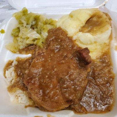 Smothered pork chop over rice, side of mashed potatoes and cabbage.