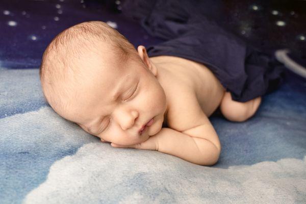 newborn posed on starry night backdrop during newborn photography session.