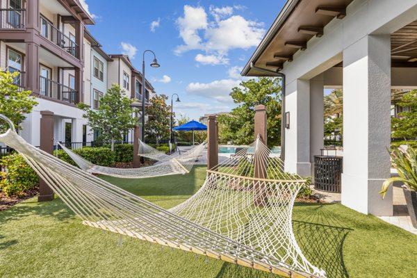 Hammock Garden with two hammocks hanging over artificial turf with the pool in the background at Lantower Grande Flats Apartments.