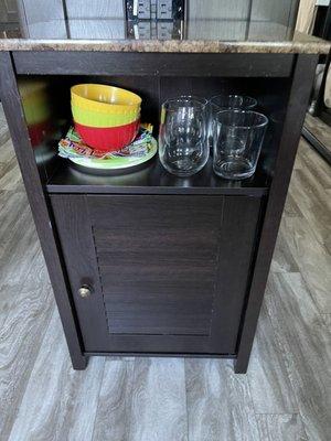 Cute cabinet that is being used to hold liquor and mixers inside and drink glasses and snack bowls and plates for happy hour!