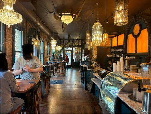 The entrance is welcoming, with a few covered tables and chairs outside the doors. The display cases are filled with DELICIOUS pastries.