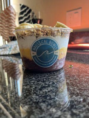 Açaí Bowl layered with açaí, mango and coconut. Topped with granola, bananas and honey.