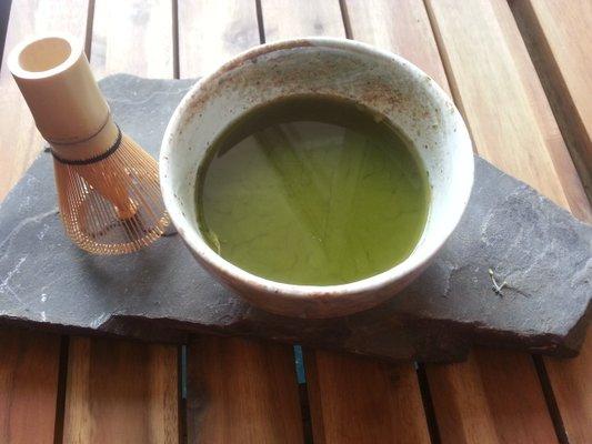 Organic "matcha" green tea served in traditional Japanese ceremonial tea cup with bamboo whisk mixer.