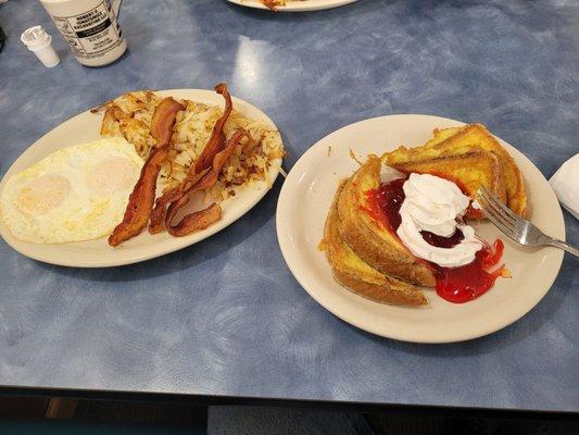 French toast with strawberries and creme along with eggs, bacon and hash browns