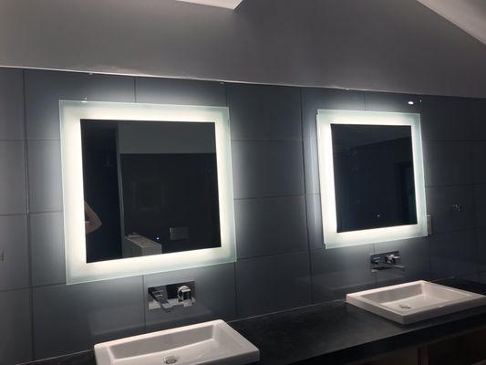 Lighted mirrors, mounted on glass tile with out of wall plumbing and black quartz vanity top.