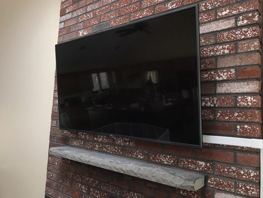 55" TV mounted above brick fireplace w/ wire mold to conceal wiring