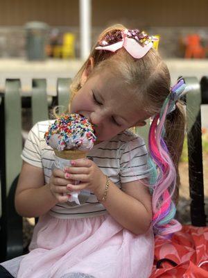 Vegan berry ice cream with rainbow sprinkles on a cake cone.