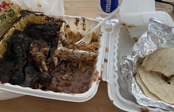 My partially-eaten takeout box with chicken in mole sauce, rice, and refried beans.