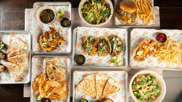 Overhead shot capturing the essence of our menu: the Cadillac Burger, cheesy Quesadillas, vibrant Tacos, fresh Salad, and more delight