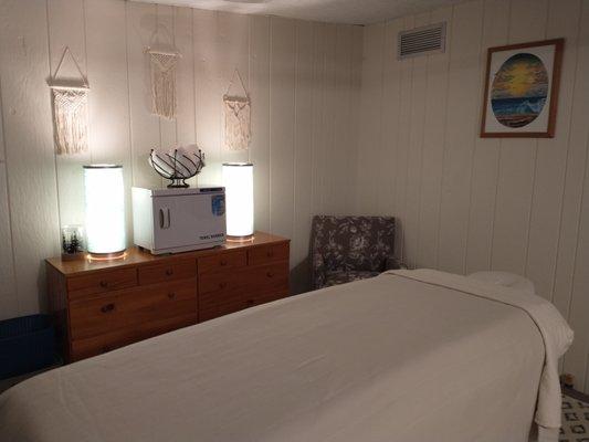 Phot of massage table, arm chair, and dresser with lamps and towel warmer.