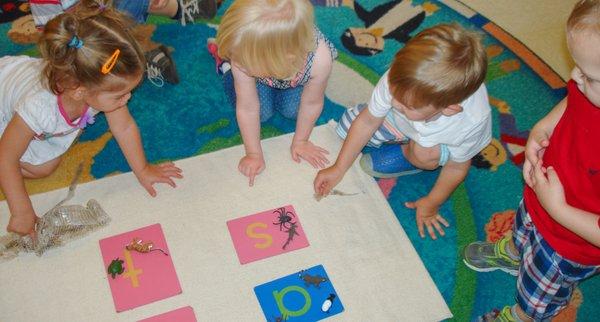 Montessori focuses on decoding language, providing individual and group lessons. Here, students are grouping objects with sandpaper letters.