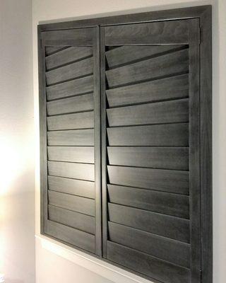 Gray stained real wood plantation shutters on an angled window.