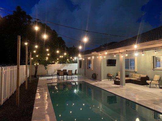 After: removed sand, created swale to protect neighbor and pool. Added grey pebbles, light post, and string lights, trimmed mamey tree.