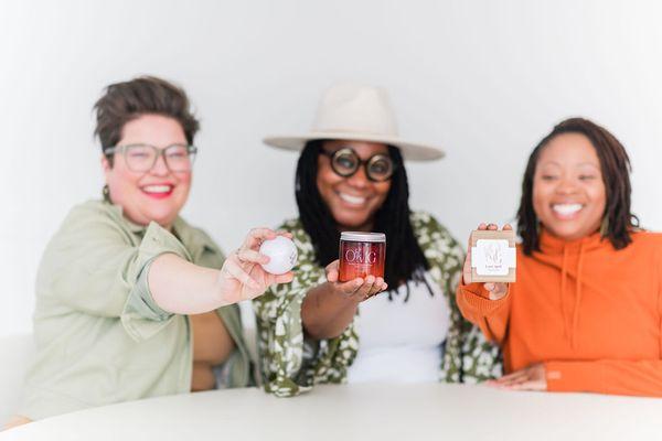 OMG founder, Shayla and clients hold her handmade bath bombs, body butter, and soap in their hands. OMG products & services are for everyone