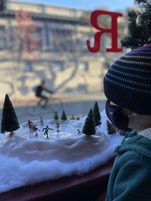 The littlest human enjoys the winter scene set up at Red Rocks, outside, a bicyclist passes. This is a quintessential Mountain View scene.