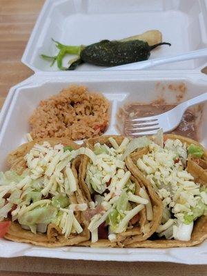 three tacos plate with the yellow corn tortillas. rice and beans chips and salsa on the side