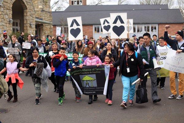 A crowd, led by children holding a Community Alliance of Tenants banner, marches.