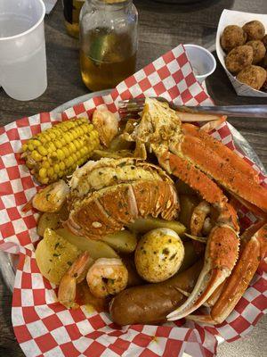 Shrimp, crab legs, lobster tail, potatoes, corn on the cob, sausage and an egg in Cajun butter.  Hush puppies on the side.