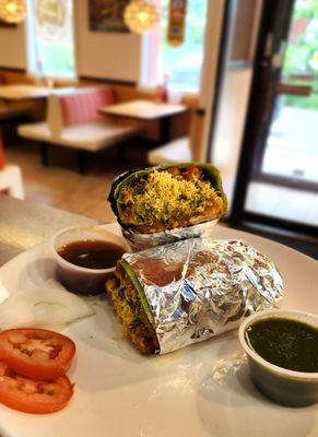 Samosa Chaat Wrap: Mashed samosa topped with savory Chana Masala, sweet tamarind chutney, diced tomatoes, onions, cilantro, & mint chutney