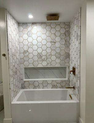 Bathroom, tub with marble tiles. Gold hardware