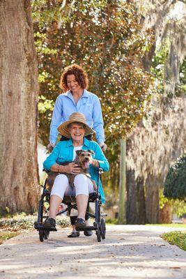 Caregiver pushing a client in a wheelchair. Both are smiling.