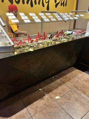 Raw food and vegetables are scattered on the counters and floor of Mongolian grill.