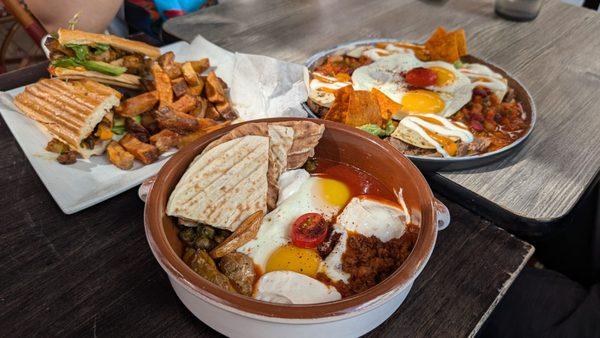 Red shakshuka in the front, left back chicken schwarma sandwich, right back brisket huevos rancheros. All delish