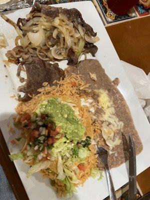 Carne Asada served with rice beans tortillas and a tortilla bowl filled with lettuce Pico and guacamole