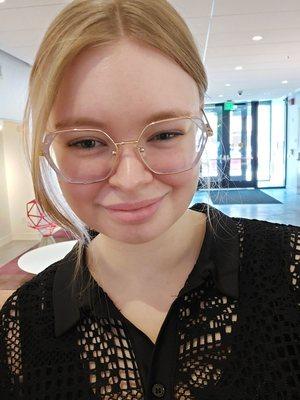 Smiling client with long blonde hair, curtain bangs, and glasses