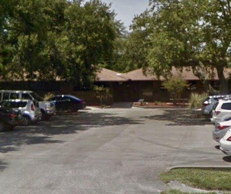 Exterior of building & parking lot, obscured to a large degree by trees.