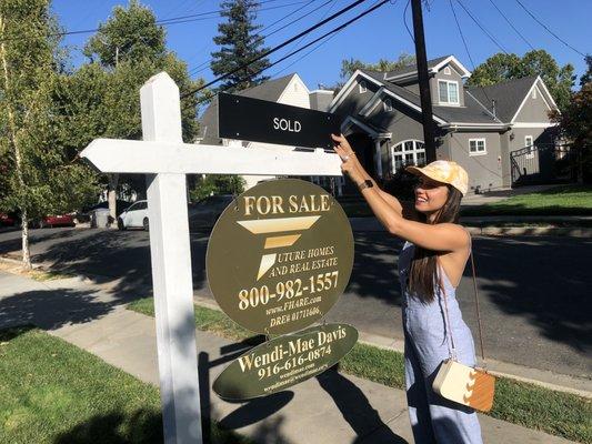 Woman placing "sold" plaque on top of a real estate sign on a front lawn.