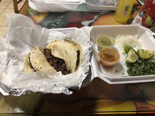 Carne asada tacos come with cilantro, white onion, limes and salsas.