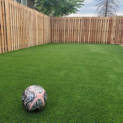 Artificial turf in yard with tall fence installation.