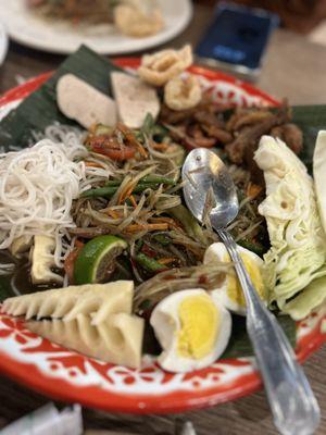 Tum Thard Lao Style papaya salad with boiled egg, moo your, vermicelli noodles, pork rinds, bamboo, and extra crispy chicken pieces.