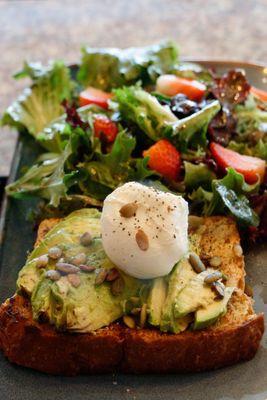 Avocado toast! On a crunchy pumpkin seed bread with pumpkin seed spread and a poached egg accompanied with rugula salad.