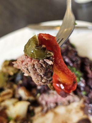 A fork holding a piece of the Steak Diane with green and red pepper.