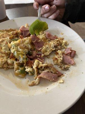 Denver omelette with chucks of raw green bell pepper and sliced lunch meat.