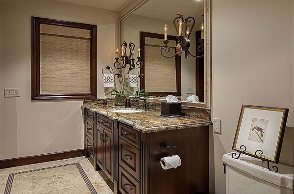 Detailed dark wood cabinetry, iron and crystal sconces, rainforest granite and mosaic inset limestone flooring make up this masculine bath