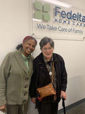 A Fedelta Home Care caregiver smiles with her client after they picked up a reward from the office