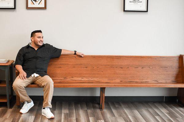 The shop owner (Eli) sitting on the waiting benches. Waiting patiently for the next patron of the barbershop to enter for a service.