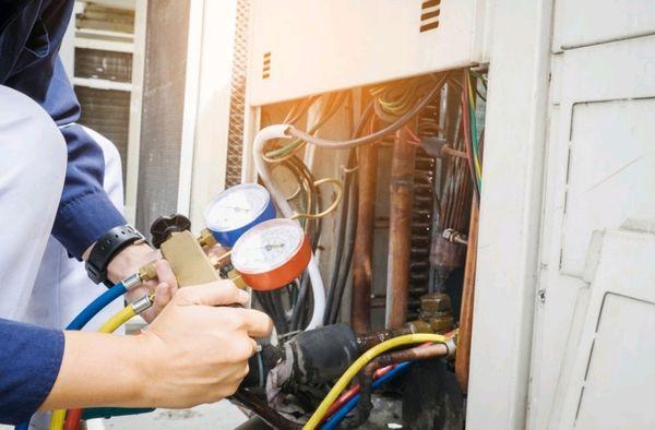 Checking refrigerant levels in an air conditioner's condenser.