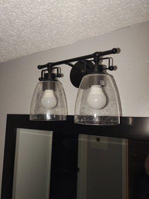 This the bathroom light fixture which is very elegant above a black framed mirror.