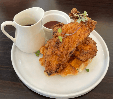 Crispy fried chicken on golden-brown waffles, drizzled with syrup and served with a side of sauce.