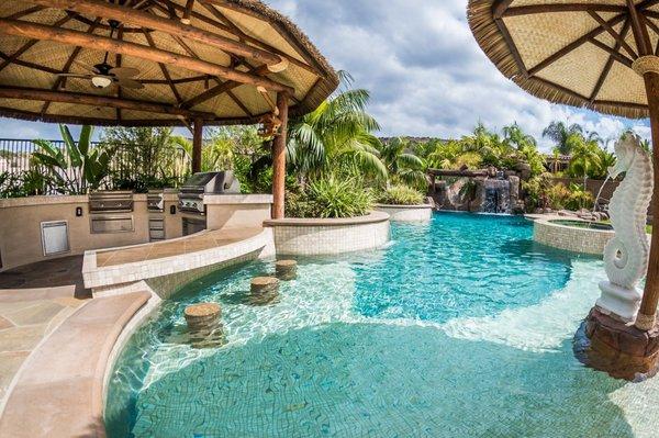 Tropical beach entry custom swimming pool with a perimeter flow spa, grotto, rock slide, and waterfalls. Outdoor kitchen with swim up bar.