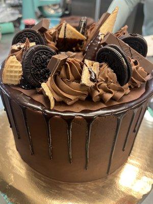 Cocoa Loco is a decadent chocolate cake with a chocolate buttercream and chocolate ganache drip. Topped with chocolate candies and cookies.