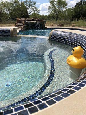 Rolled edge of hot tub looking out to grotto waterfall (kids can hide under it on a seating ledge)