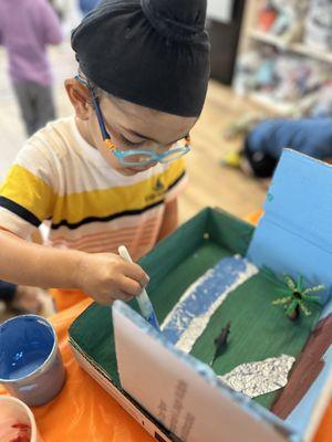 A three year old student is engaged in the prehistoric village box enhancing imagination, and concentration skills.